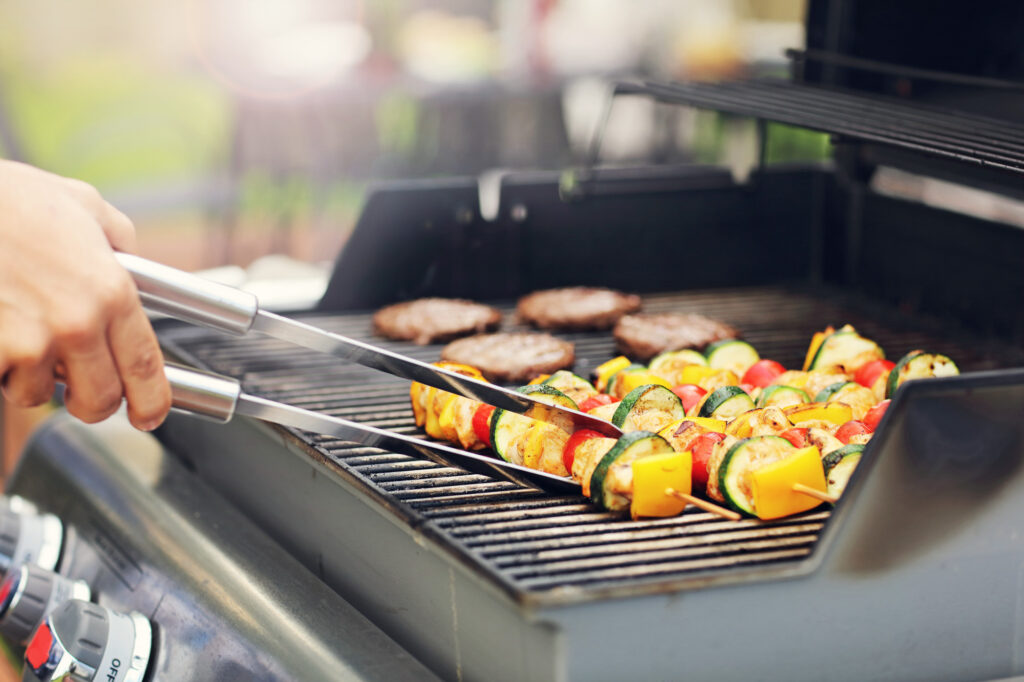 Close up of skewers and burgers being cooked on grill