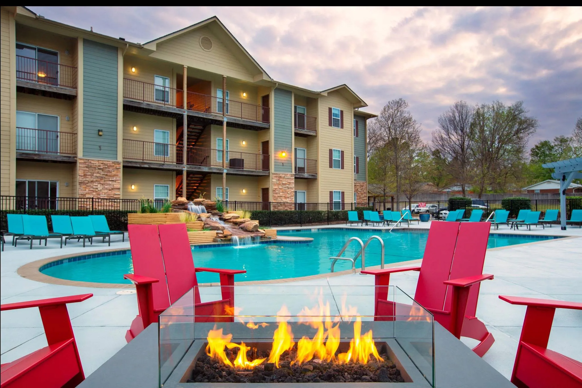 Fire pit with chairs surrounding and pool and apartment building shown behind