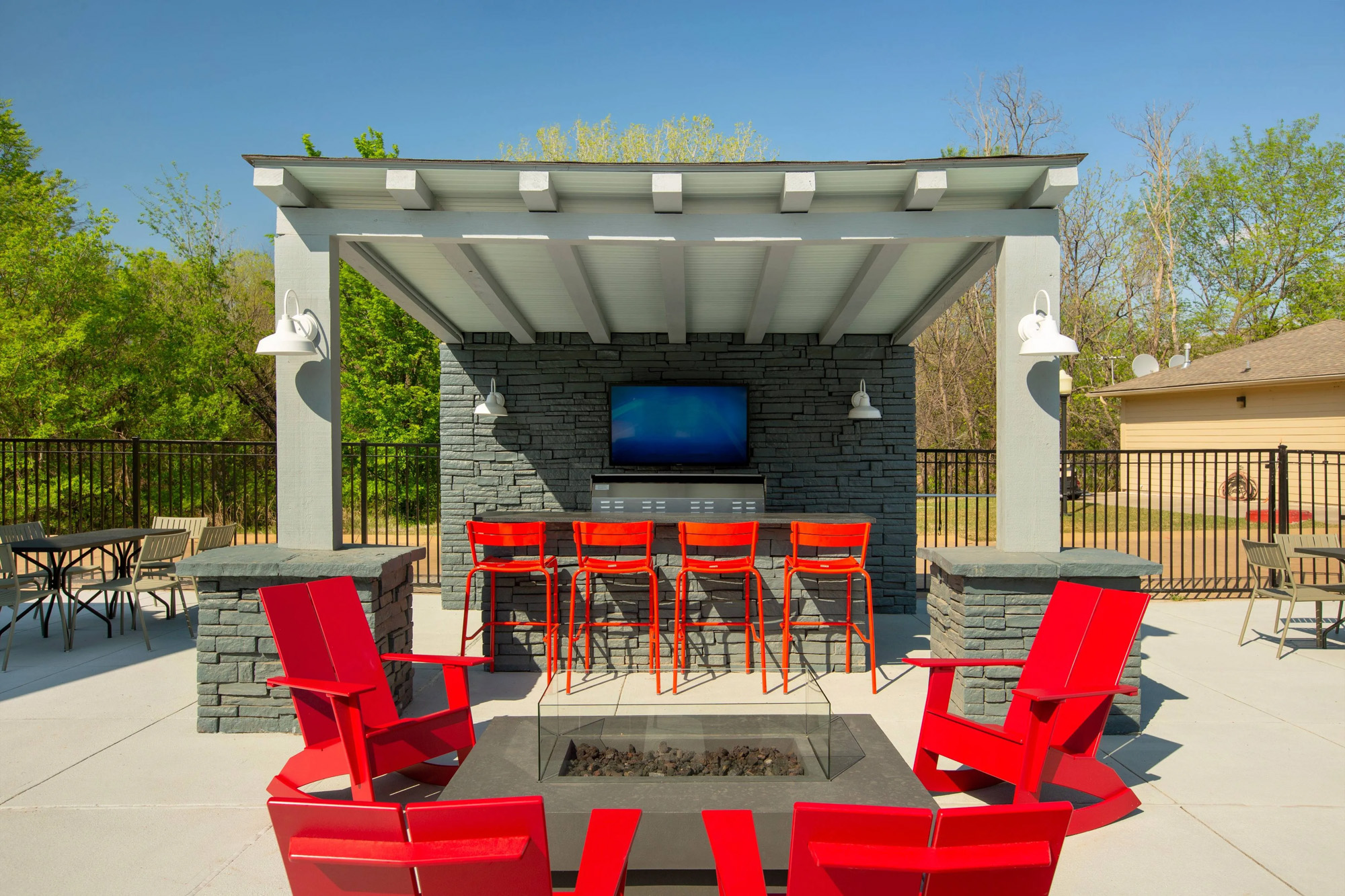 Fire pit with chairs surrounding behind big TV and outdoor bar area