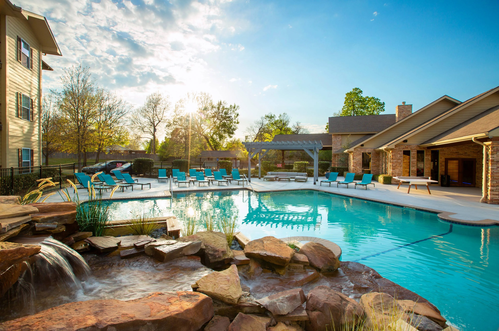 Resort style pool with lounge chairs surrounding and rock waterfall next to apartment building